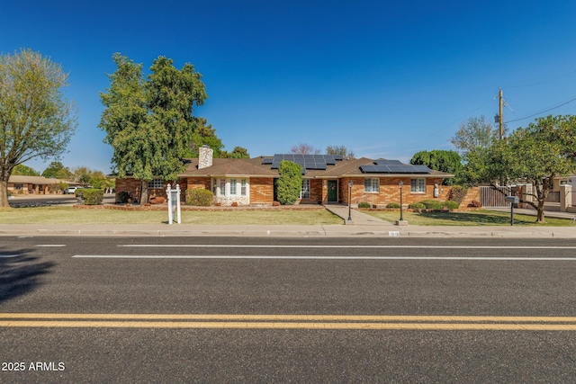 ranch-style house with brick siding, solar panels, a chimney, fence, and a front yard