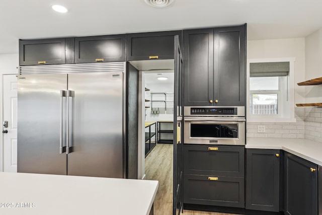 kitchen with light wood-style flooring, light countertops, appliances with stainless steel finishes, backsplash, and open shelves