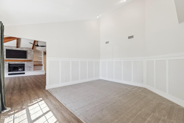 empty room with lofted ceiling, a brick fireplace, wood finished floors, and a decorative wall