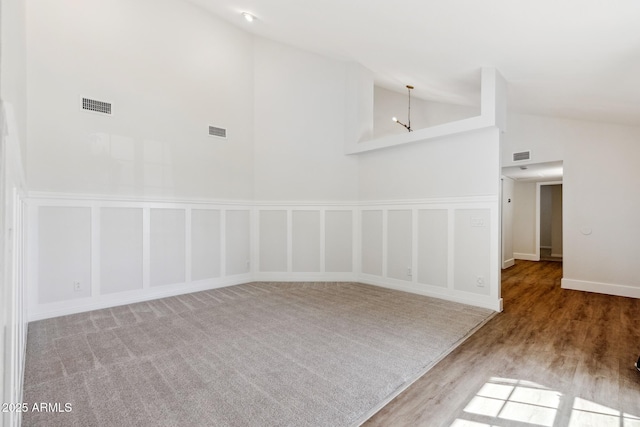 empty room with high vaulted ceiling, visible vents, a decorative wall, and a notable chandelier