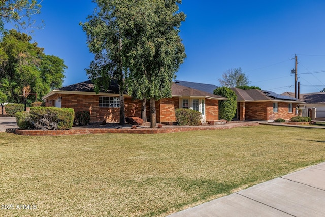 ranch-style home featuring a garage, a front yard, roof mounted solar panels, and brick siding