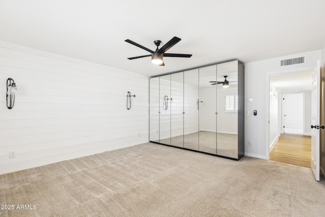 unfurnished bedroom featuring a closet, visible vents, carpet flooring, wood walls, and ceiling fan