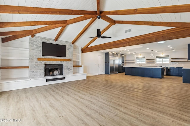 unfurnished living room featuring beam ceiling, a fireplace, visible vents, ceiling fan, and light wood-type flooring