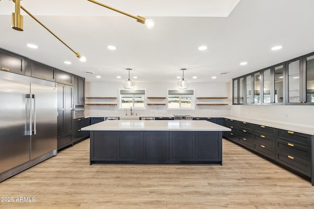 kitchen featuring appliances with stainless steel finishes, a center island, light countertops, open shelves, and a sink