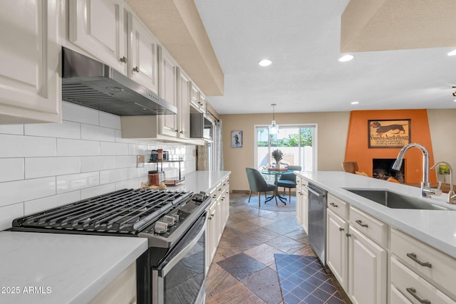 kitchen with recessed lighting, under cabinet range hood, appliances with stainless steel finishes, stone tile floors, and a sink