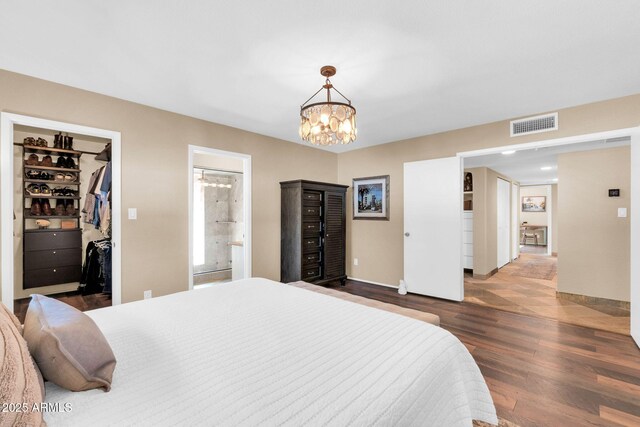 bedroom featuring a notable chandelier, connected bathroom, a walk in closet, visible vents, and wood finished floors