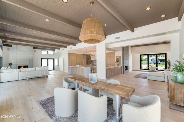 dining room featuring beam ceiling, a fireplace, light hardwood / wood-style floors, and french doors