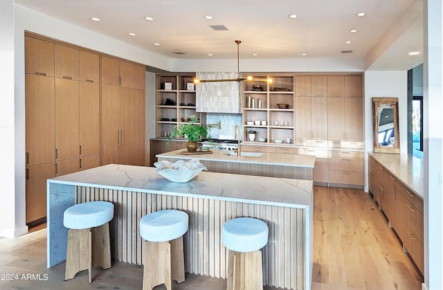 kitchen featuring a kitchen bar, sink, decorative light fixtures, light hardwood / wood-style floors, and a large island