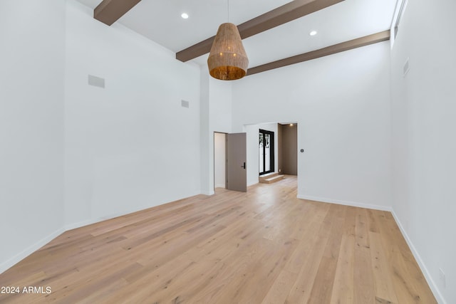 unfurnished room featuring beam ceiling, light wood-type flooring, and a high ceiling