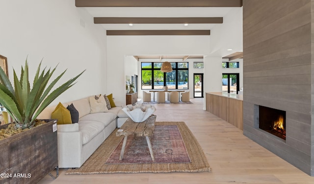 living room featuring a fireplace, beam ceiling, light hardwood / wood-style flooring, and french doors