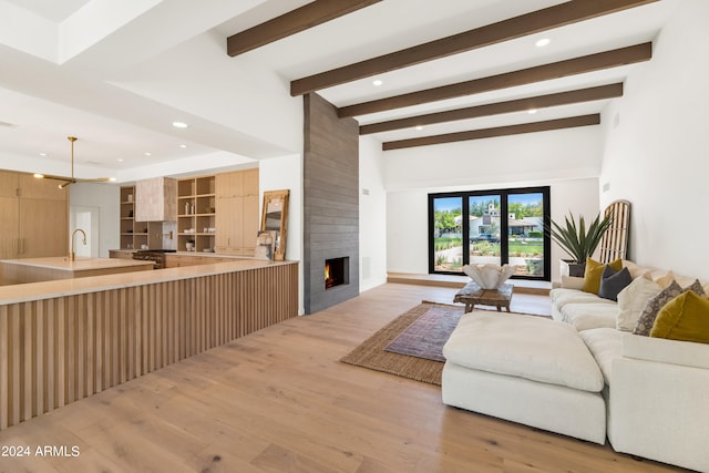 living room featuring beamed ceiling, light hardwood / wood-style floors, sink, and a fireplace