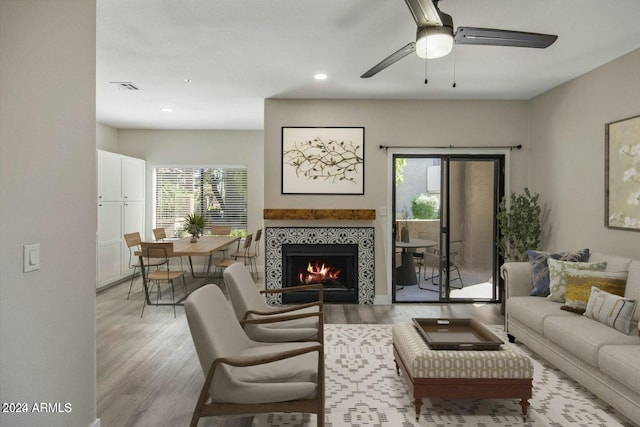 living room featuring a tiled fireplace, ceiling fan, and light hardwood / wood-style floors