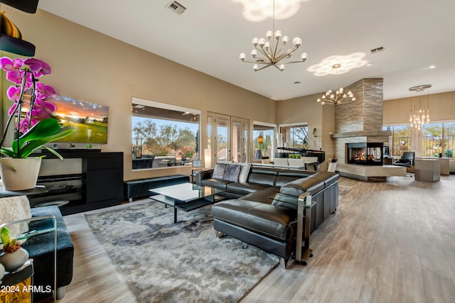 living room featuring a wealth of natural light, light hardwood / wood-style flooring, a multi sided fireplace, and a notable chandelier