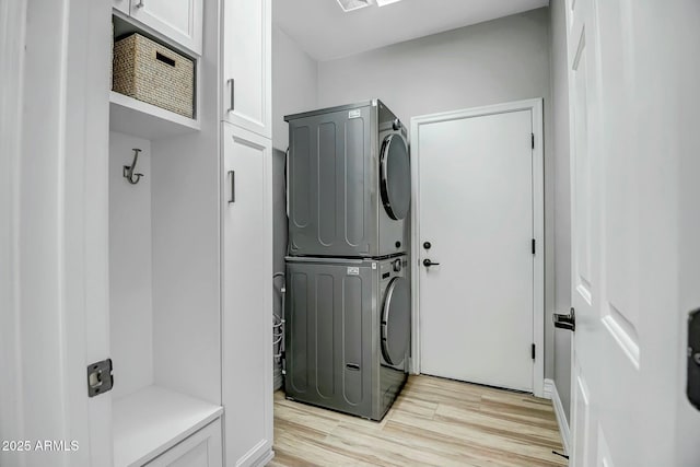 clothes washing area featuring light hardwood / wood-style flooring, stacked washer and dryer, and cabinets