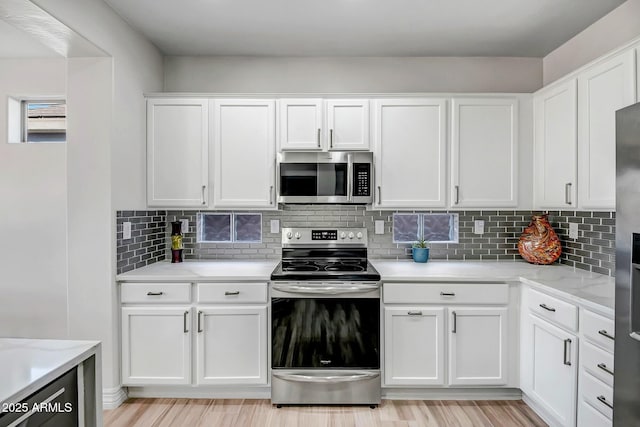 kitchen featuring white cabinets, stainless steel appliances, backsplash, light wood-type flooring, and light stone counters