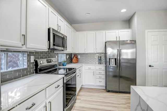 kitchen with white cabinetry, appliances with stainless steel finishes, backsplash, and light stone counters