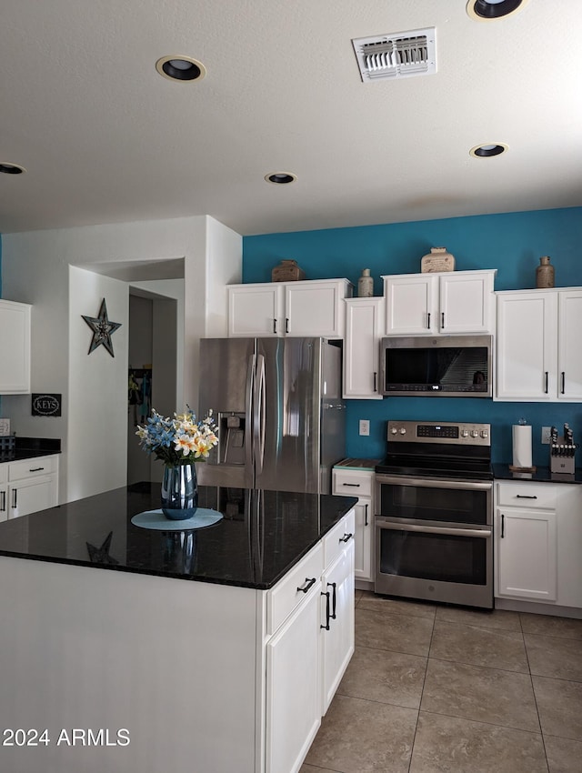 kitchen with dark stone counters, tile patterned floors, stainless steel appliances, and white cabinetry