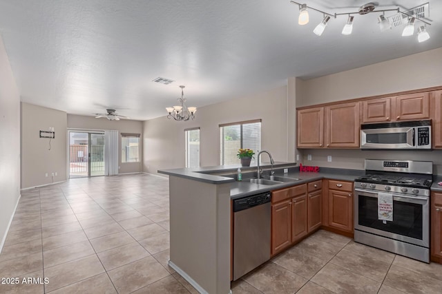 kitchen featuring a sink, open floor plan, appliances with stainless steel finishes, brown cabinetry, and dark countertops