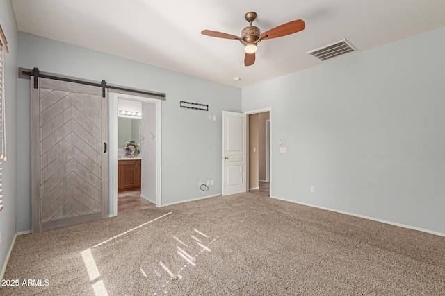 unfurnished bedroom featuring a barn door, visible vents, a ceiling fan, carpet, and ensuite bath