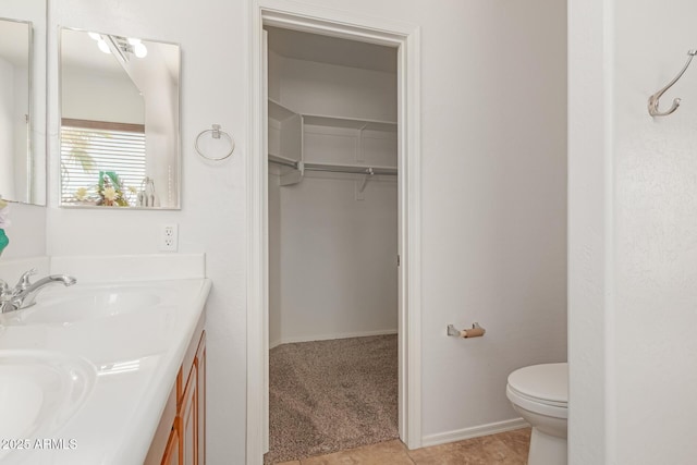 full bath featuring a walk in closet, double vanity, toilet, a sink, and tile patterned floors