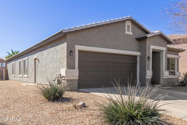 view of side of property featuring an attached garage, driveway, a tile roof, and stucco siding