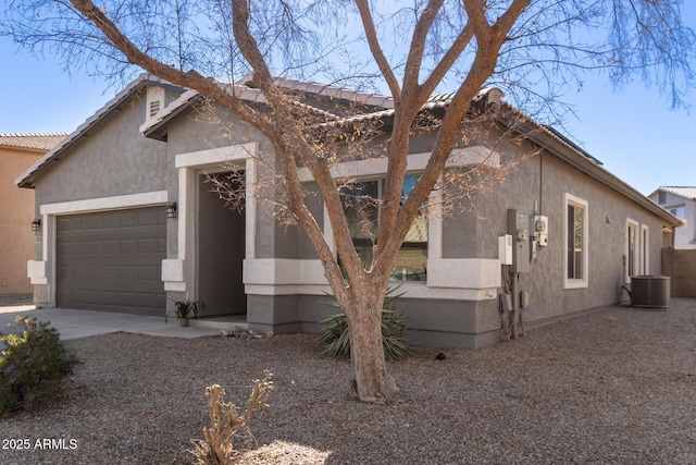 view of front of house featuring an attached garage, driveway, central AC unit, and stucco siding