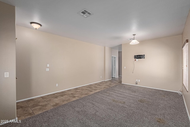 spare room featuring baseboards, visible vents, dark colored carpet, and dark tile patterned flooring