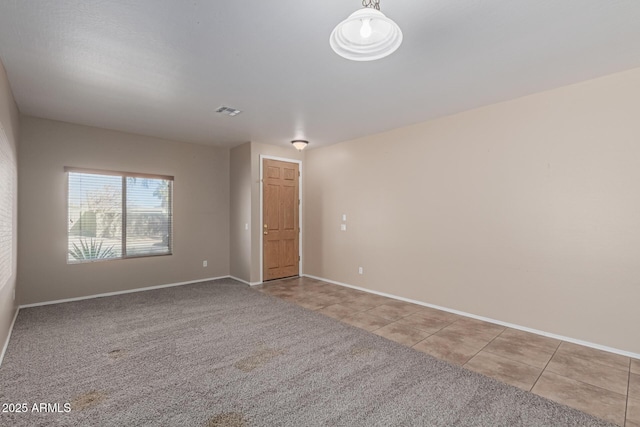 unfurnished room with light tile patterned floors, baseboards, visible vents, and light colored carpet