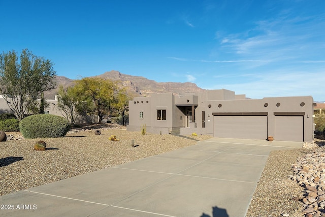 pueblo revival-style home featuring driveway, a garage, a mountain view, and stucco siding