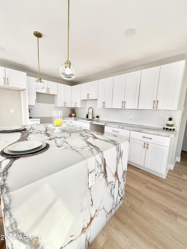 kitchen featuring light wood-type flooring, a kitchen island, pendant lighting, light stone countertops, and white cabinets