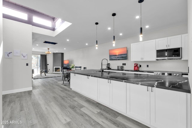 kitchen with a sink, light wood-style floors, white cabinetry, stainless steel microwave, and decorative light fixtures