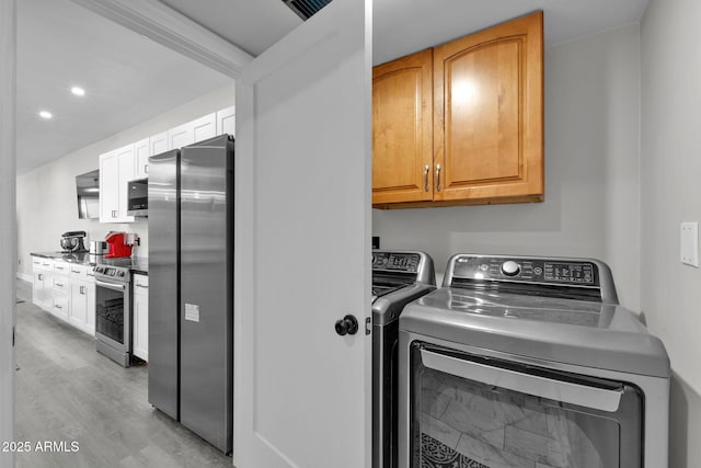 clothes washing area with washer and dryer, cabinet space, and light wood-type flooring