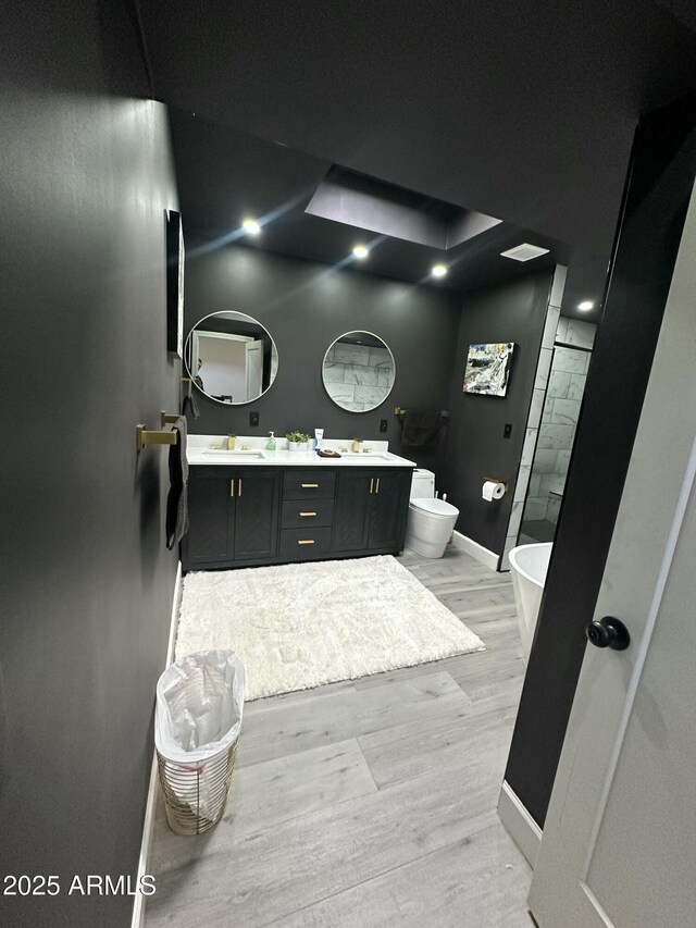 full bathroom featuring baseboards, double vanity, wood finished floors, a soaking tub, and a sink