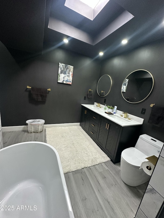 full bathroom featuring wood finished floors, a tray ceiling, a freestanding tub, a skylight, and toilet