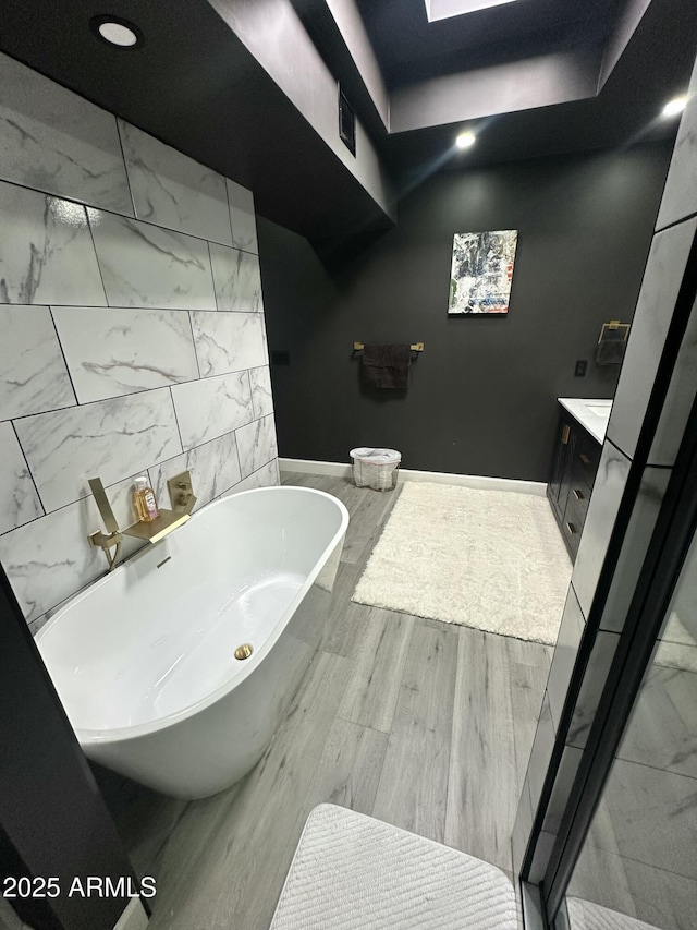 full bath featuring baseboards, a freestanding bath, wood finished floors, and vanity