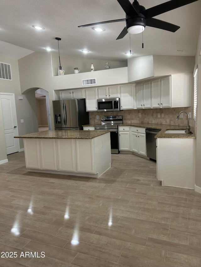 kitchen with appliances with stainless steel finishes, a kitchen island, decorative backsplash, sink, and hanging light fixtures