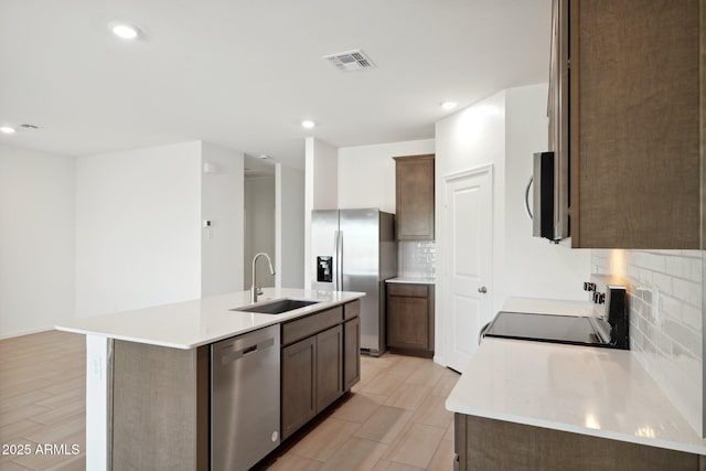 kitchen featuring decorative backsplash, stainless steel appliances, a kitchen island with sink, sink, and light hardwood / wood-style flooring