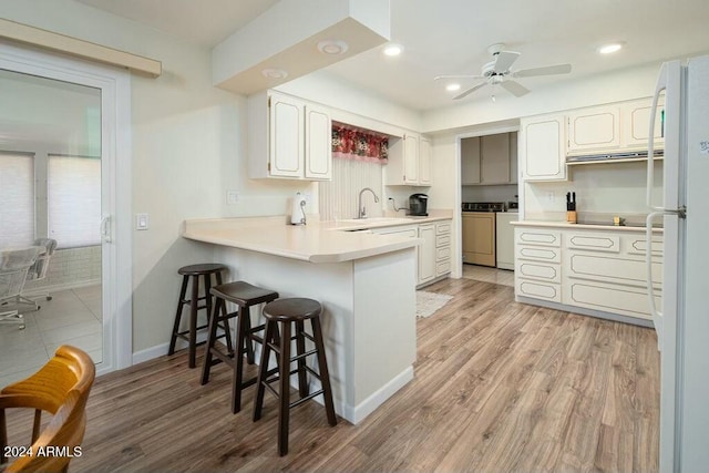 kitchen featuring a kitchen breakfast bar, white refrigerator, washer and dryer, light wood-type flooring, and kitchen peninsula