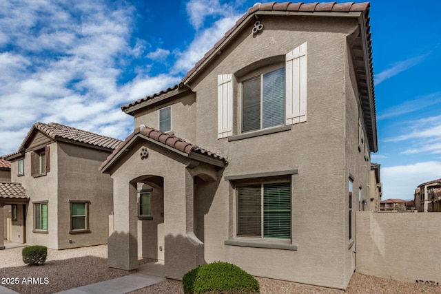 view of front of house with stucco siding, a tiled roof, and fence