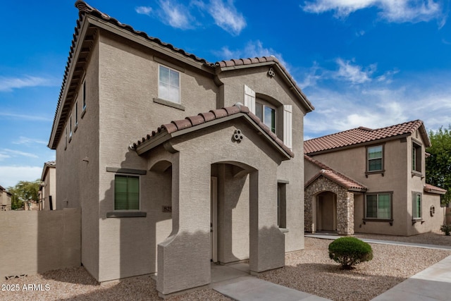 mediterranean / spanish home with stucco siding, fence, and a tile roof