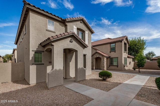 mediterranean / spanish-style home featuring stucco siding, fence, and a tile roof