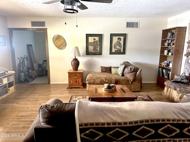 living room featuring a textured ceiling, light wood-type flooring, and ceiling fan