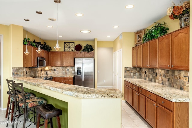 kitchen with hanging light fixtures, a breakfast bar area, decorative backsplash, light tile patterned floors, and stainless steel appliances