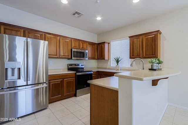 kitchen featuring kitchen peninsula, appliances with stainless steel finishes, sink, light tile patterned flooring, and a breakfast bar