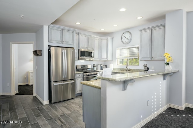 kitchen featuring light stone countertops, appliances with stainless steel finishes, a breakfast bar area, and kitchen peninsula