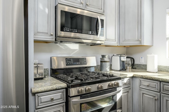 kitchen with light stone counters, stainless steel appliances, and gray cabinetry