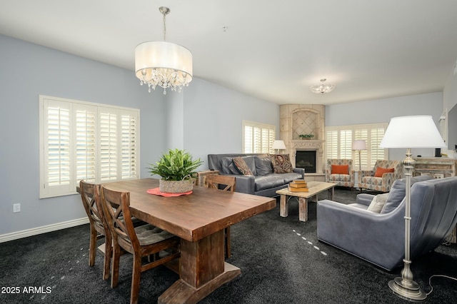 dining area with dark carpet, a large fireplace, and an inviting chandelier