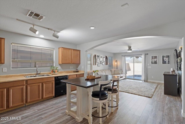 kitchen with dishwasher, sink, a kitchen bar, light hardwood / wood-style floors, and a textured ceiling