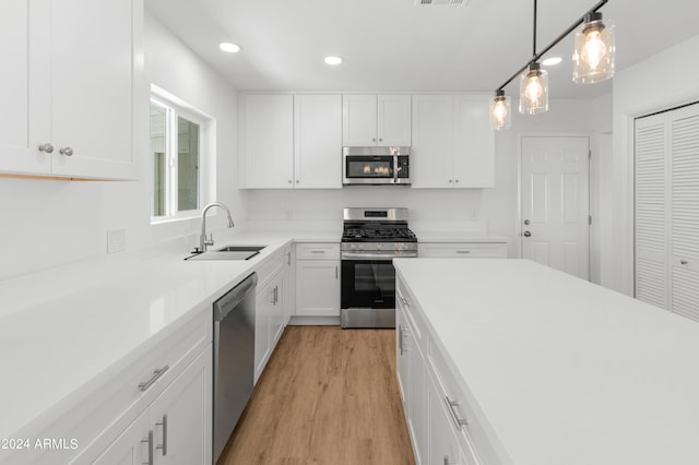 kitchen with sink, decorative light fixtures, white cabinetry, appliances with stainless steel finishes, and light hardwood / wood-style floors