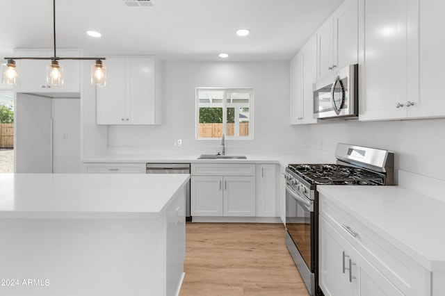 kitchen featuring white cabinetry, pendant lighting, stainless steel appliances, light wood-type flooring, and sink